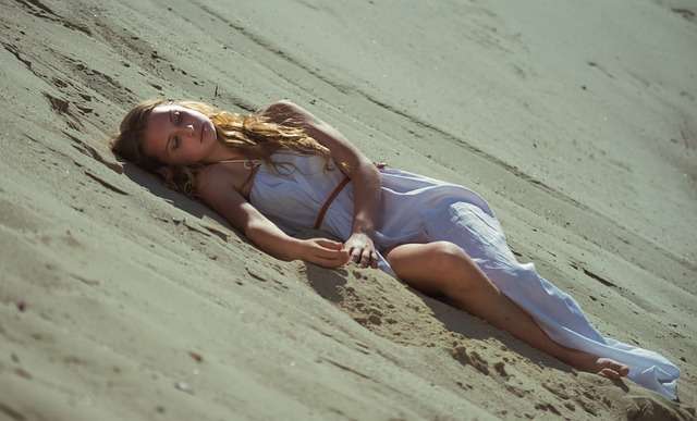 alt=mujer tumbada en la arena de la playa con expresión triste que mejora con plantas adaptógenas